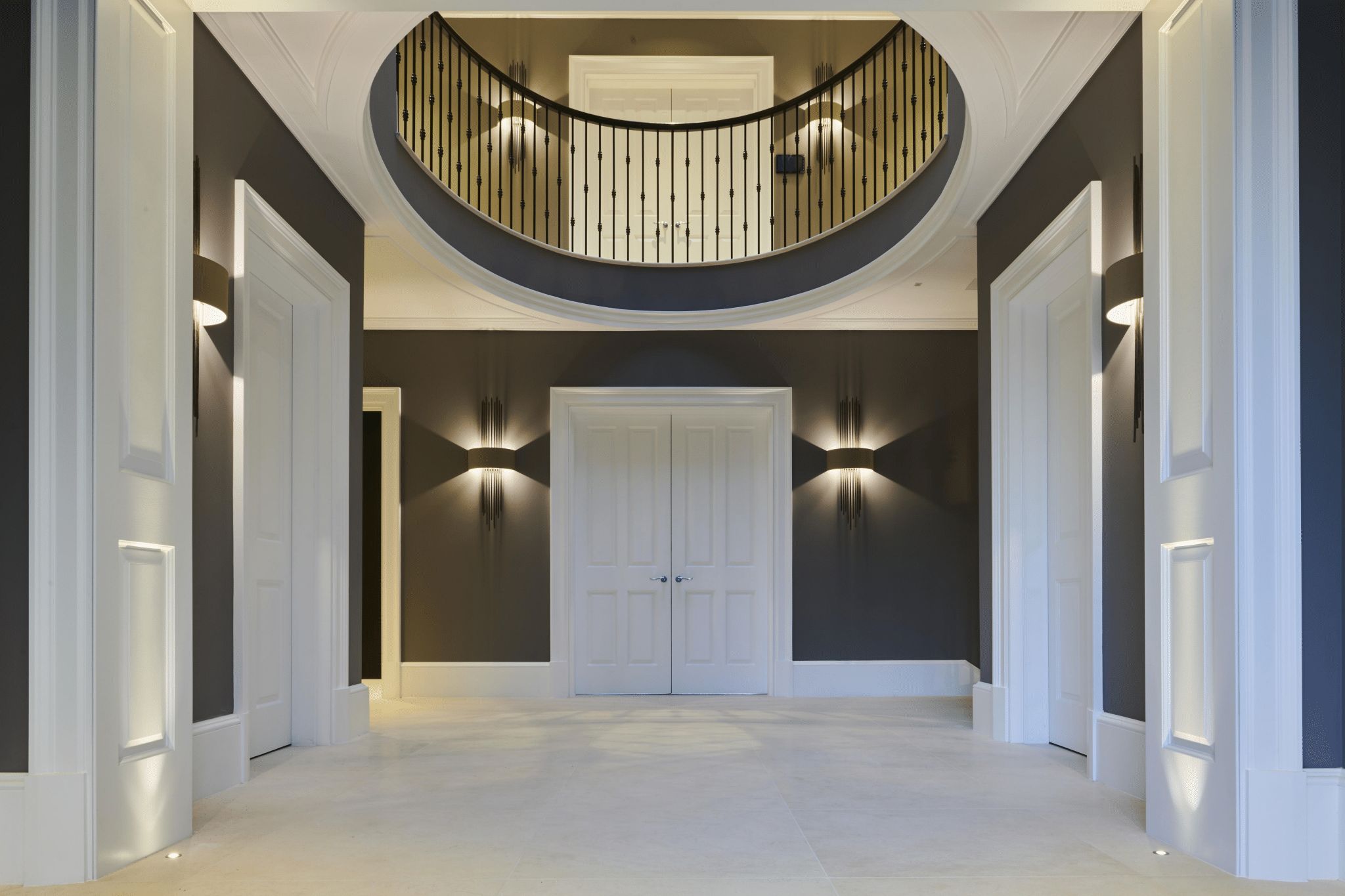 Double-height entrance hall with dark feature walls, detailed mouldings, and a curved balcony above.