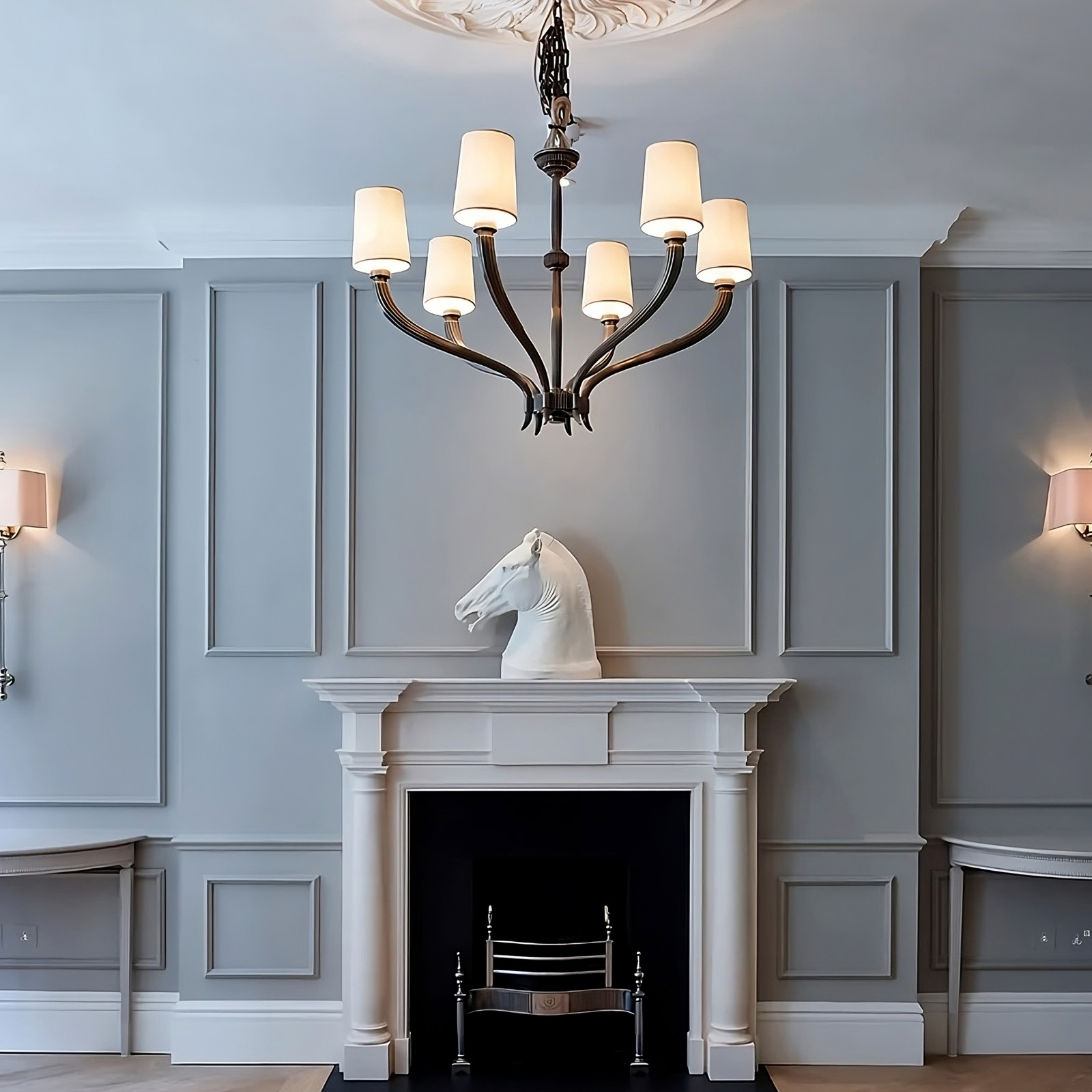 Refined Georgian-style room with soft grey panelled walls, central chandelier, and equestrian sculpture above the fireplace.