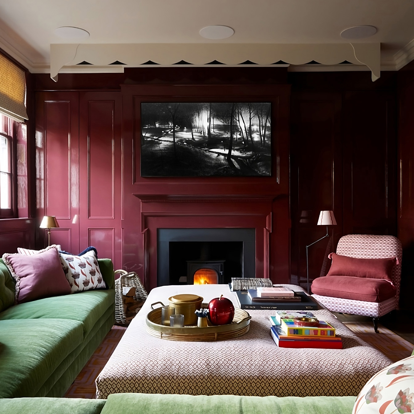 Deep red panelled living room with green velvet sofas, layered soft furnishings, and eclectic styling in a period West London home.