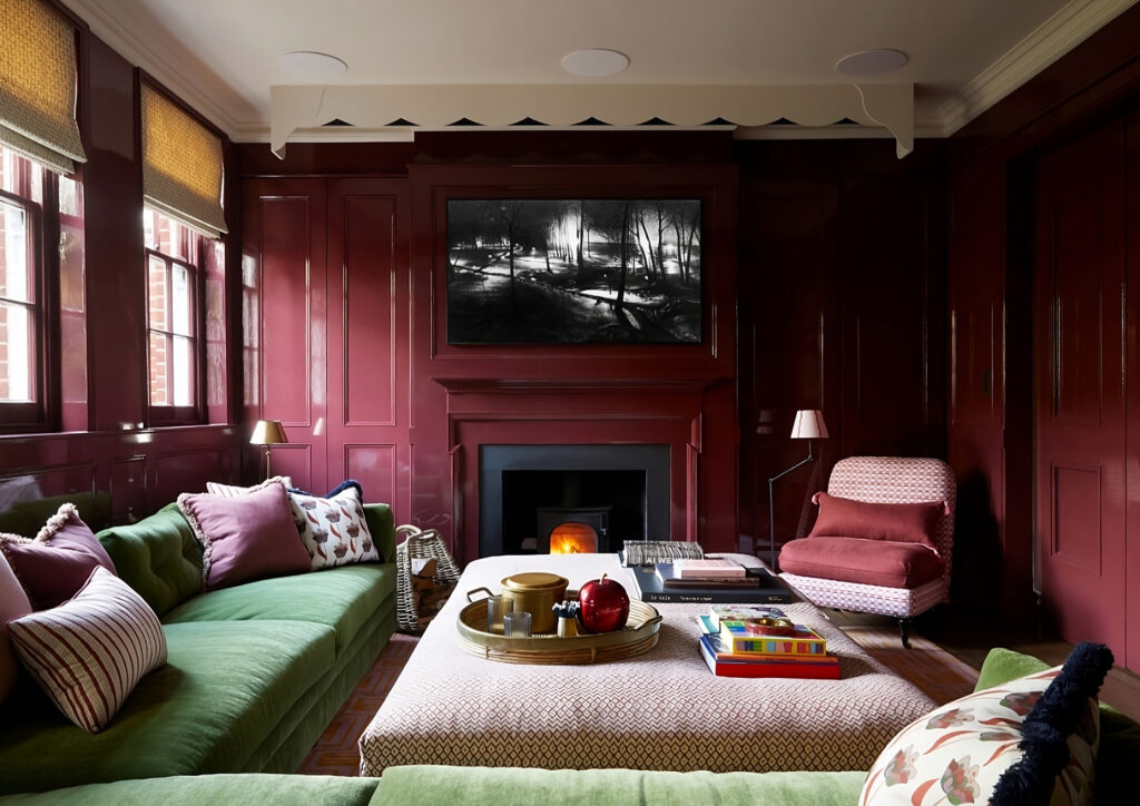 Luxurious living room with high-gloss burgundy walls, green velvet sofas, and a contemporary fireplace.
