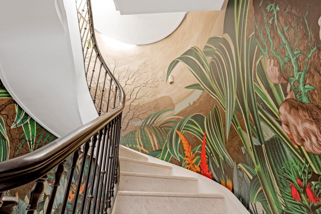 Curved staircase with detailed tropical mural spanning the stairwell wall, showcasing brushwork and bold colours.