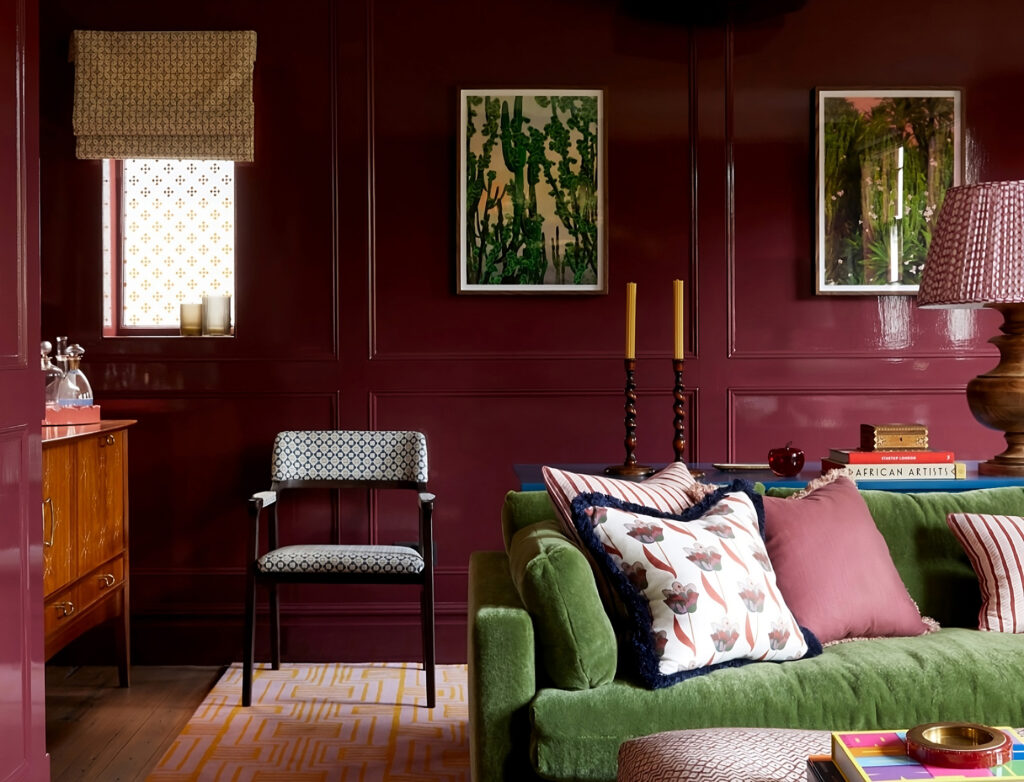 Stylish corner of a burgundy-painted lounge with a green velvet sofa, abstract rug, curated books, and contemporary art.