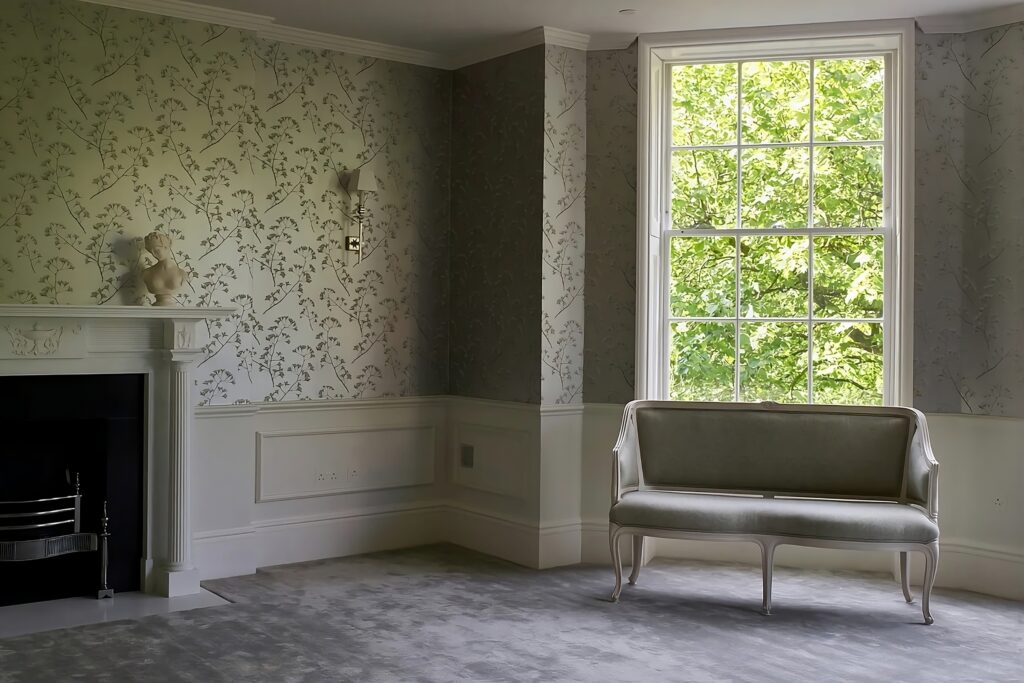 Refined Georgian sitting room with botanical silk wallcovering, bespoke joinery, and soft neutral tones framing a tall window.